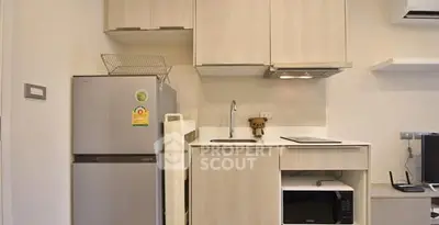 Modern compact kitchen with light wood cabinets and stainless steel appliances.