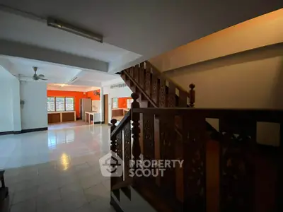 Spacious open-plan living area with intricate wooden staircase and bright orange accent wall.