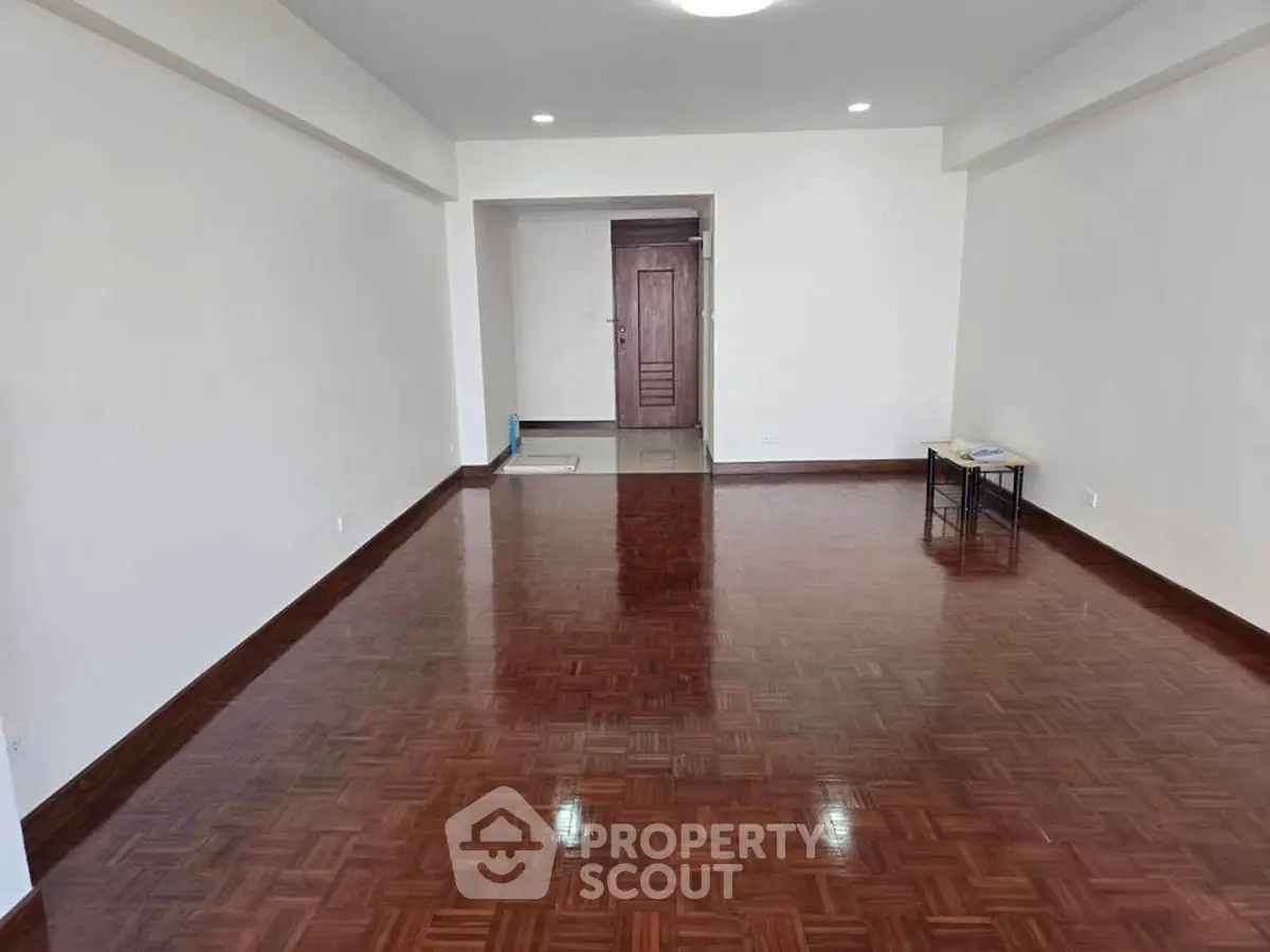 Spacious empty room with polished wooden floors and white walls, ready for customization.