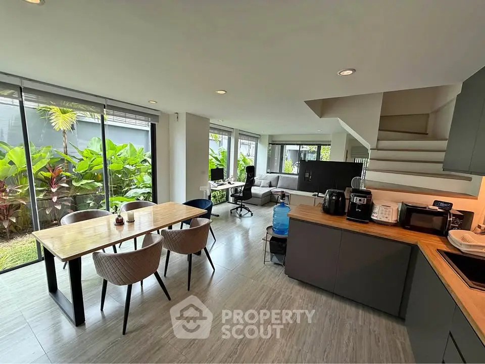 Modern open-plan living and dining area with garden view, featuring sleek kitchen and stylish furnishings.