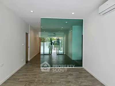 Spacious modern living room with large glass partition and sleek wooden flooring.