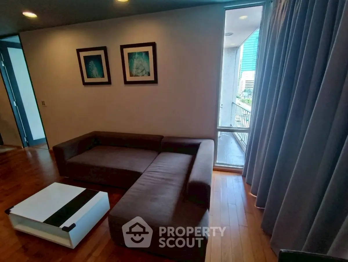 Cozy living room with modern sofa and coffee table, featuring wooden flooring and balcony access.