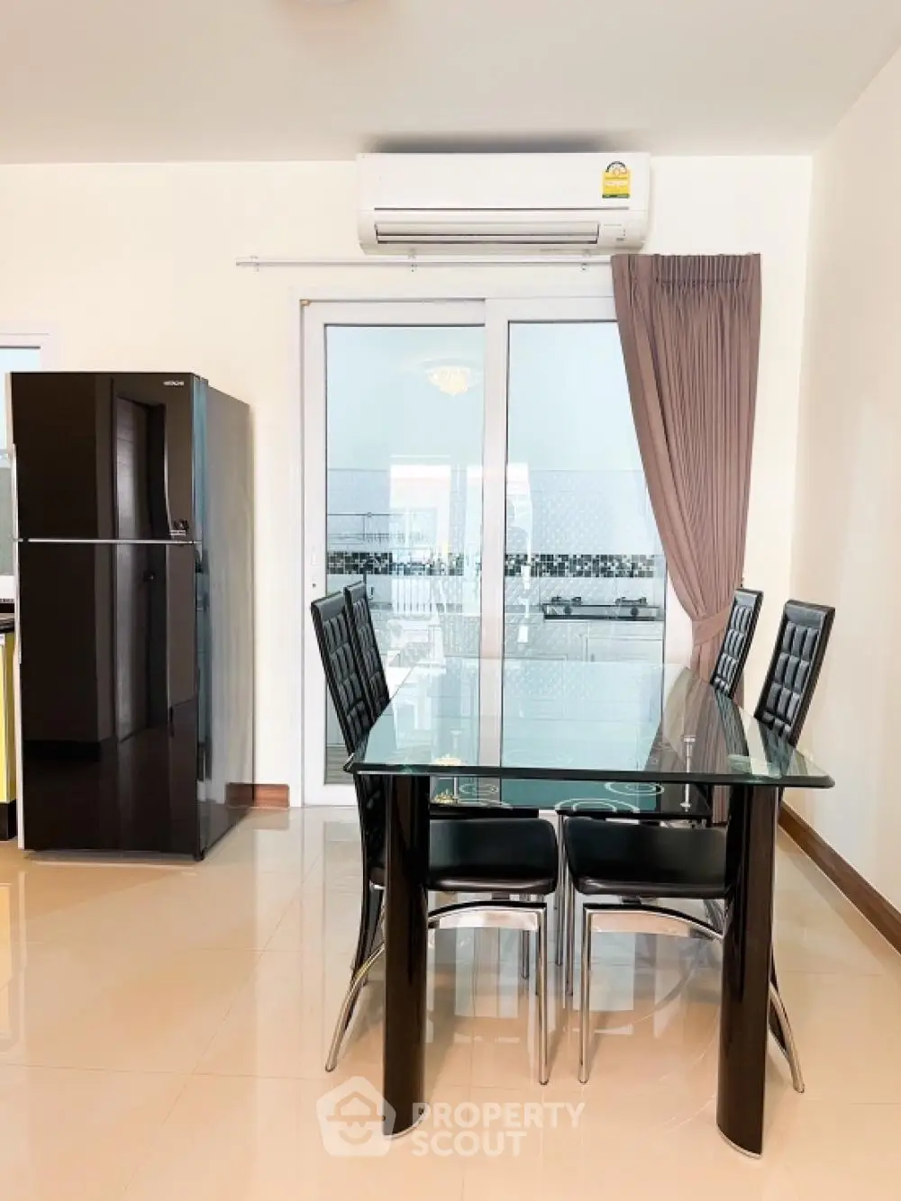 Modern dining area with sleek black chairs and glass table, complemented by a large fridge and natural light from balcony doors.