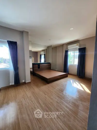 Spacious bedroom with wooden flooring and large windows for natural light