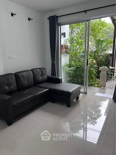 Modern living room with sleek black leather sofa and garden view through sliding glass doors.
