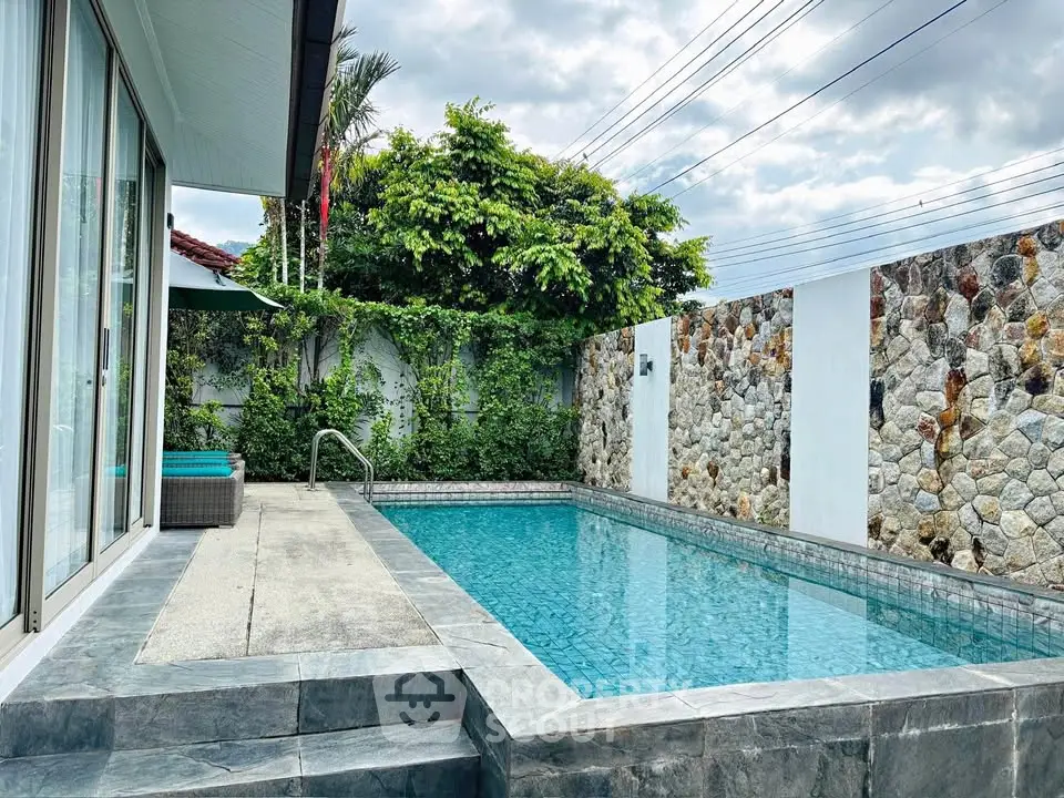 Luxurious private pool with stone wall and lush greenery in modern villa setting.