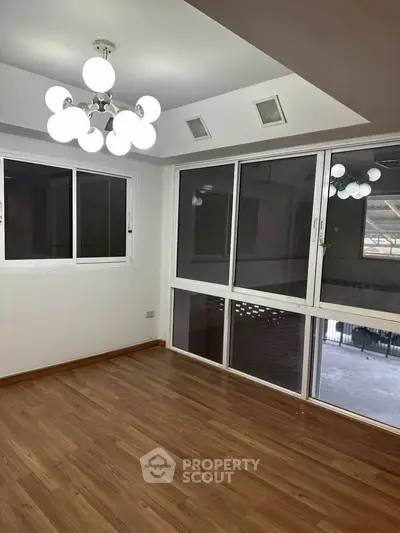 Spacious room with wooden flooring and modern lighting, featuring large windows for natural light.