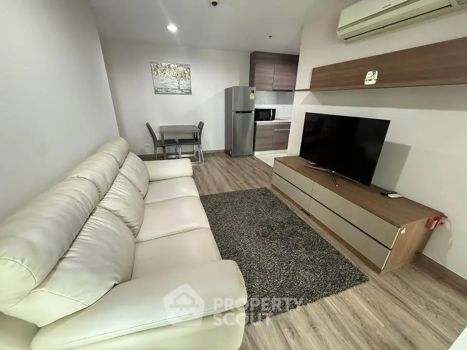 Modern living room with cozy sofa, flat-screen TV, and sleek kitchen area in open layout apartment.