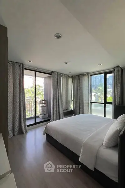 Spacious bedroom with large windows and balcony access in modern apartment.
