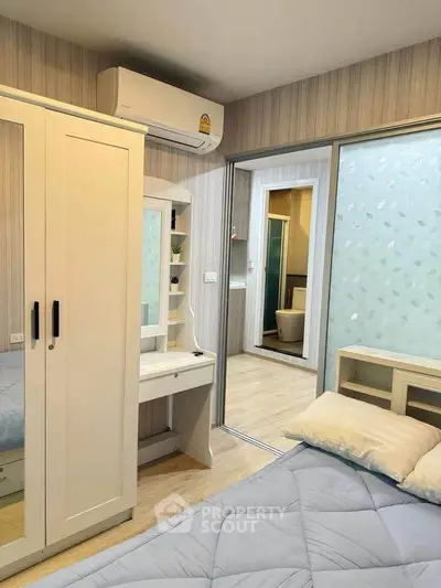 Cozy bedroom with modern decor and air conditioning, featuring a wardrobe and a glimpse into the bathroom.