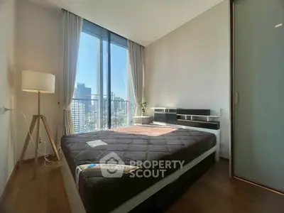 Modern bedroom with large window offering city view, featuring sleek furniture and natural light.