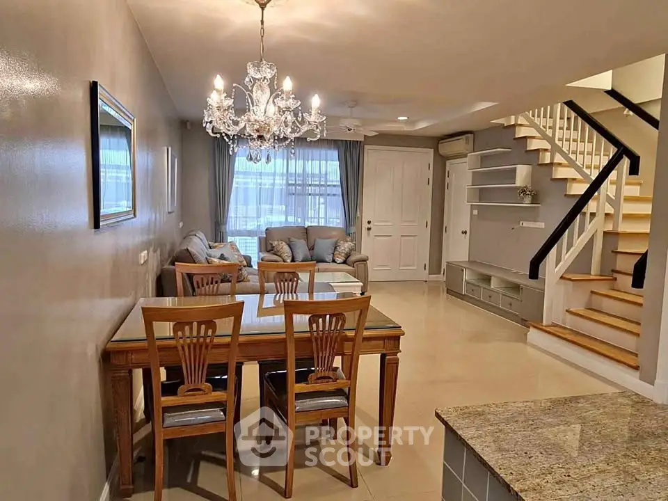 Elegant living room with chandelier, dining area, and staircase in a cozy home setting.