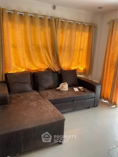 Cozy living room with plush brown sofa and warm golden curtains, perfect for relaxation.