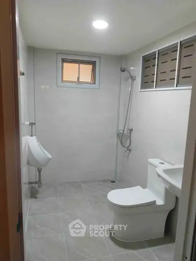Modern bathroom with sleek fixtures and neutral tiles, featuring a shower and toilet.