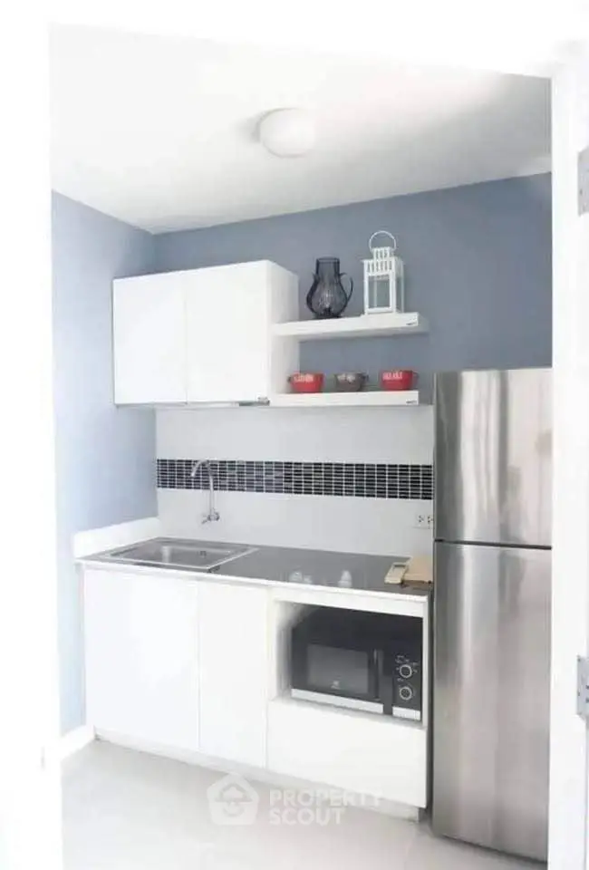 Modern compact kitchen with sleek white cabinets and stainless steel fridge in a cozy apartment.