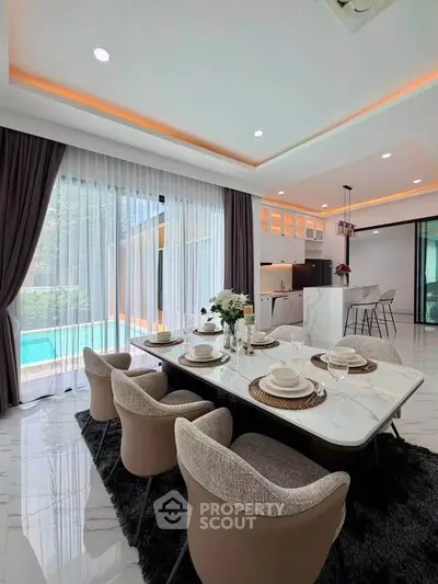 Luxurious open-plan dining and kitchen area with pool view, elegant decor, and modern furnishings.