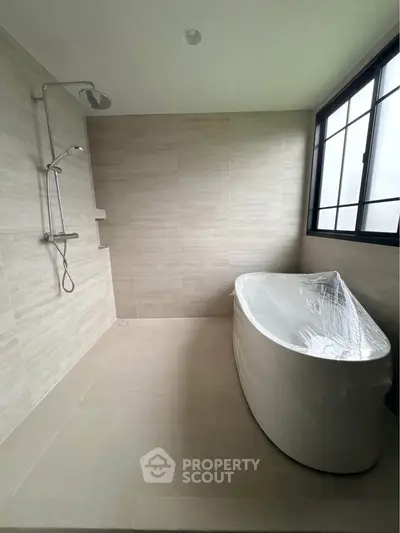 Modern bathroom with sleek bathtub and rainfall shower, featuring large window for natural light.