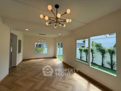 Spacious living room with modern chandelier and large windows overlooking a private garden.