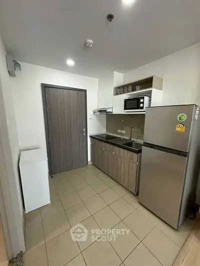 Modern compact kitchen with stainless steel fridge and microwave in cozy apartment.