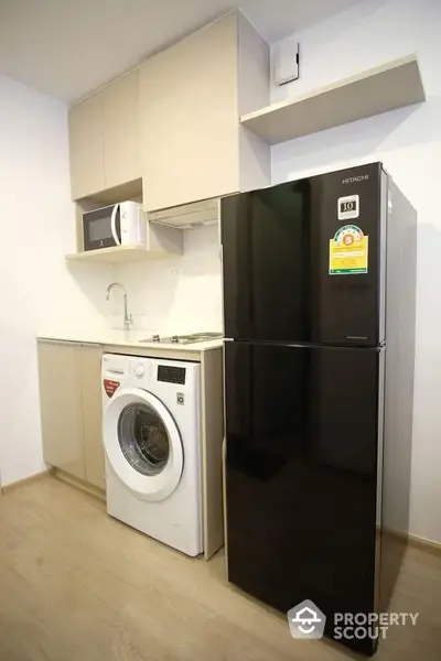 Compact and modern kitchenette with sleek black refrigerator, built-in washing machine, and microwave, perfect for urban living.