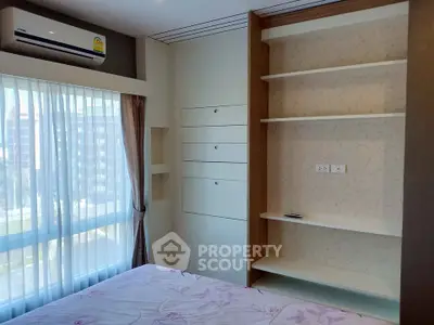 Modern bedroom with built-in shelves and air conditioning, featuring large window with city view.