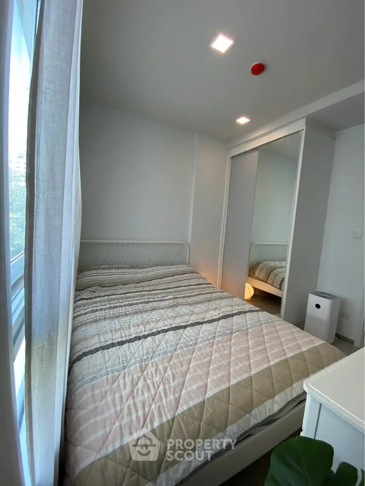 Cozy bedroom with modern decor and ample natural light from large window.