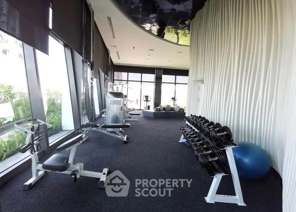 Modern gym with state-of-the-art equipment and floor-to-ceiling windows in luxury building.