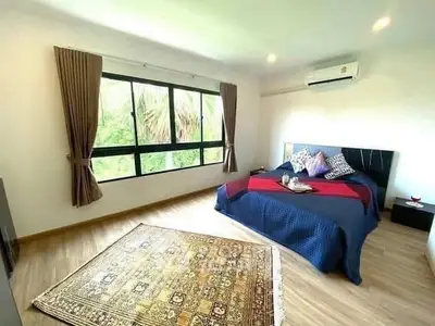 Spacious bedroom with large window and modern decor, featuring a cozy bed and elegant rug.