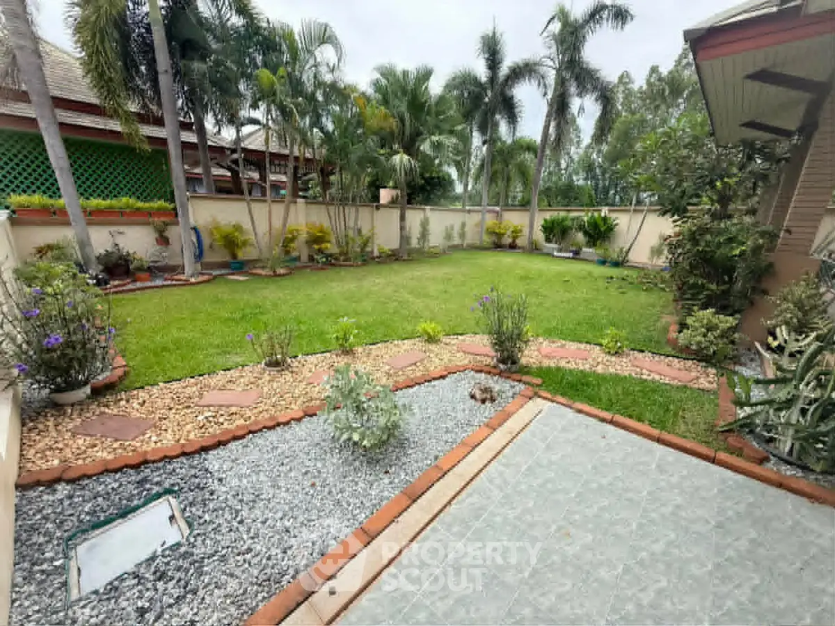 Spacious garden with lush greenery and palm trees in a serene residential setting.