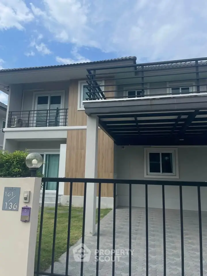 Modern two-story house with balcony and gated driveway in a serene neighborhood.