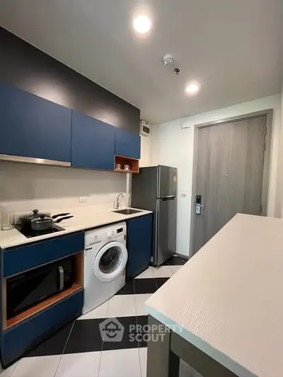 Modern kitchen with blue cabinets, washing machine, and fridge in a compact layout.