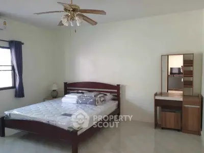 Spacious bedroom with ceiling fan and natural light, featuring a wooden bed and dresser.