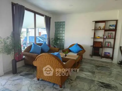 Charming living room with wicker furniture and marble flooring, featuring large windows for natural light.