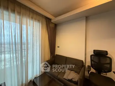 Cozy living room with modern sofa and office chair by large window with sheer curtains.