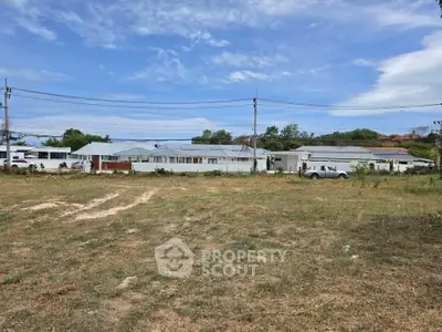 Expansive land with potential for development, featuring clear skies and existing structures in the background.