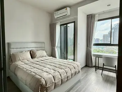 Modern bedroom with city view, featuring a cozy bed and a study nook by the window.
