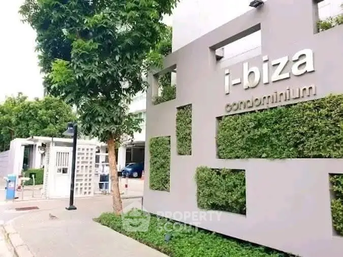 Modern condominium entrance with lush greenery and stylish signage.