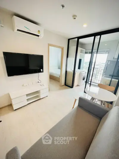 Modern living room with balcony view, featuring sleek furniture and integrated kitchen appliances.