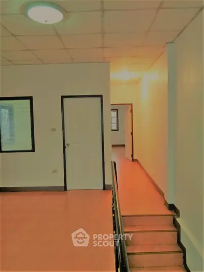 Spacious commercial hallway with warm lighting, terracotta tiled flooring, and multiple doors leading to offices or units.
