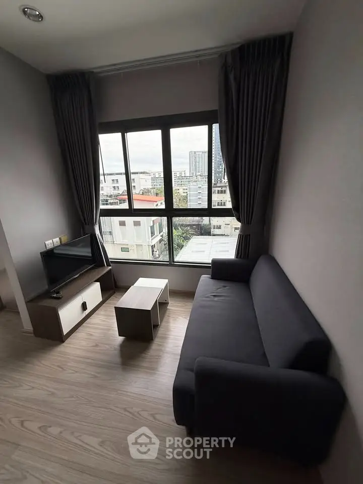 Modern living room with city view, featuring sleek furniture and large window.