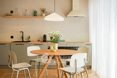 Modern kitchen with round wooden table and stylish chairs, featuring sleek cabinetry and elegant lighting.