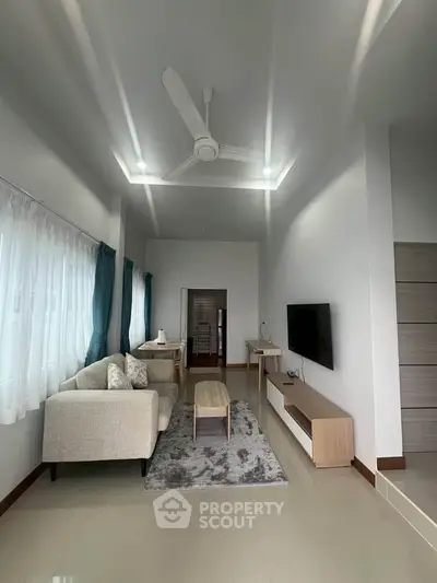 Modern living room with sleek furniture and ceiling fan, featuring natural light and minimalist design.