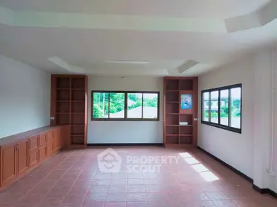 Spacious room with large windows and built-in wooden cabinets, offering natural light and serene views.