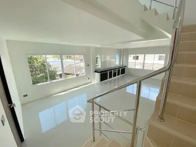 Spacious modern living room with large windows and sleek staircase in a bright home.