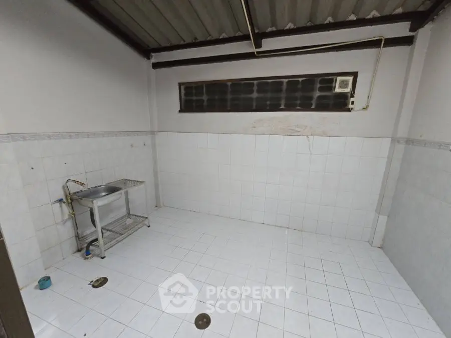Spacious tiled utility area with sink and plumbing, ideal for laundry or storage use.