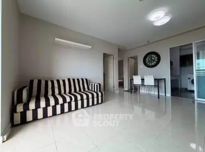 Spacious living room with modern striped sofa and dining area in open layout apartment.
