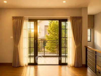 Spacious living room with large windows opening to a balcony, offering a serene view of greenery.