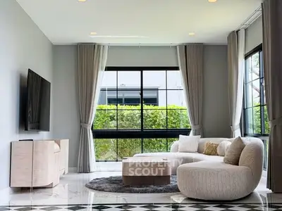Modern living room with stylish furniture and large windows offering garden views.