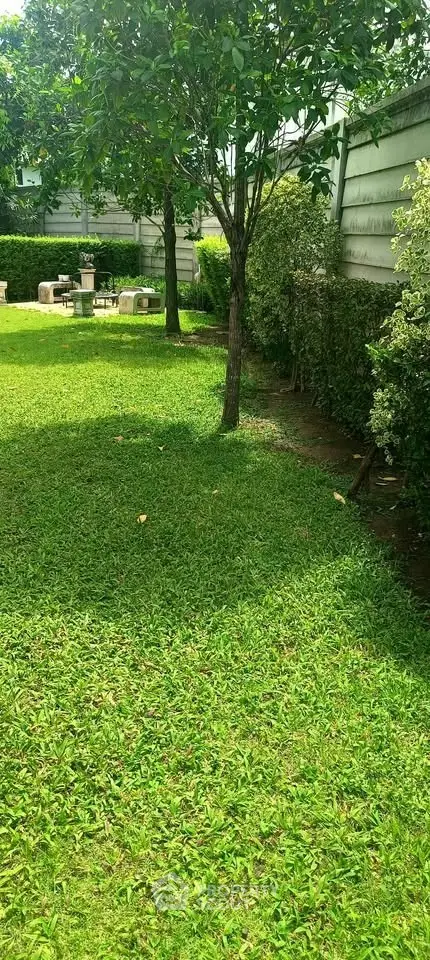 Lush green garden with trees and outdoor seating, perfect for relaxation and gatherings.