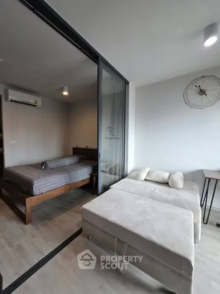 Modern studio apartment with glass partition, cozy bed, and stylish decor.